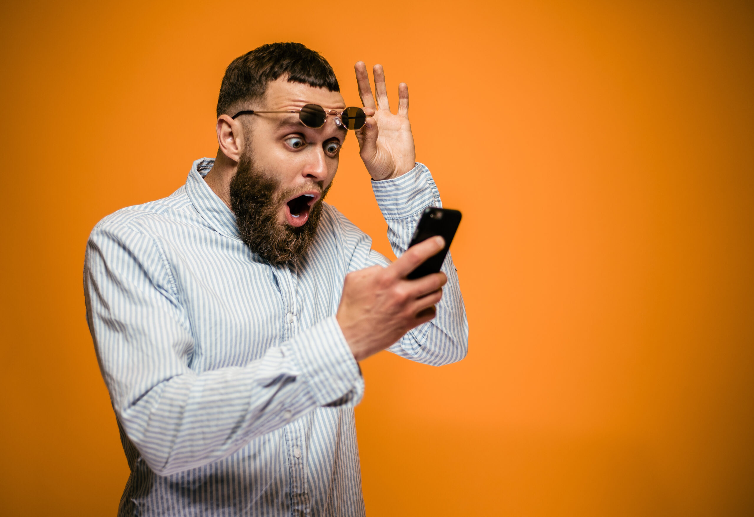 Shocked hipster man hold on eye glasses and looking at the phone. emotional male can't believe in sales in web store. blank space for your text.