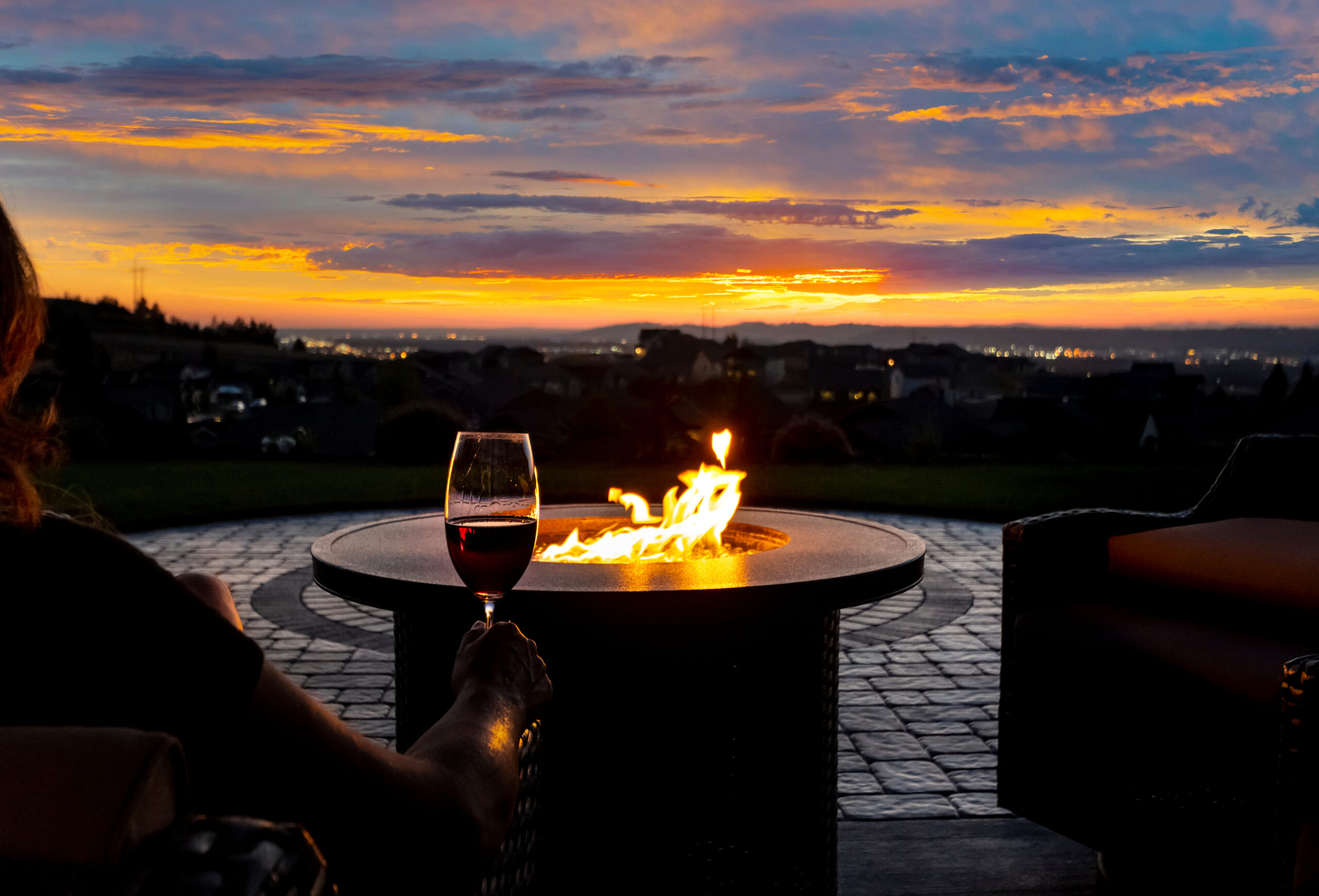 A woman drinks a glass of wine in front of a fire pit on the lux